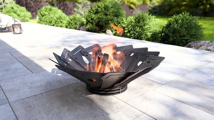 Modern outdoor fire pit with flames surrounded by green landscaping on a patio.