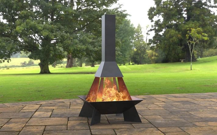 Stylish outdoor chiminea with flames, set on a stone patio surrounded by greenery.