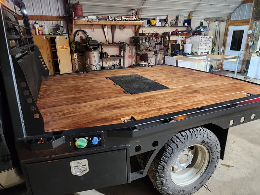 Pickup truck bed with a wooden surface, parked inside a workshop with tools in the background.